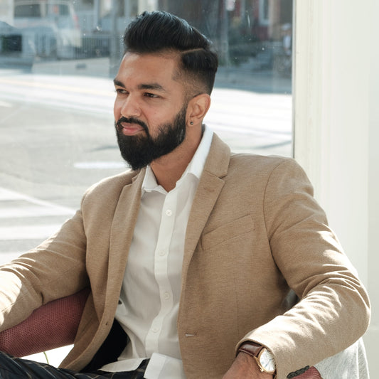 Young man with beard sits and smiles with hair and beard shaped and cut.